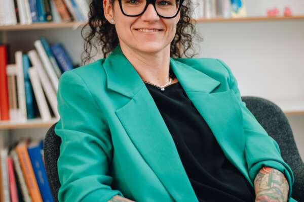 Susanne Breuer sitzt auf einem Stuhl vor einem Bücherregal.