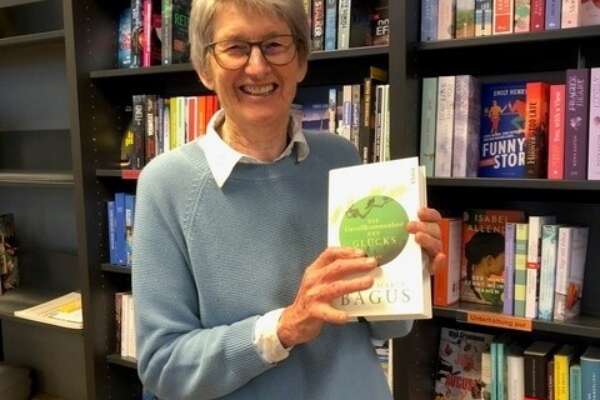 Marianne Beutler steht vor einem Bücherregal, hält ein Buch in den Händen und lächelt in die Kamera.